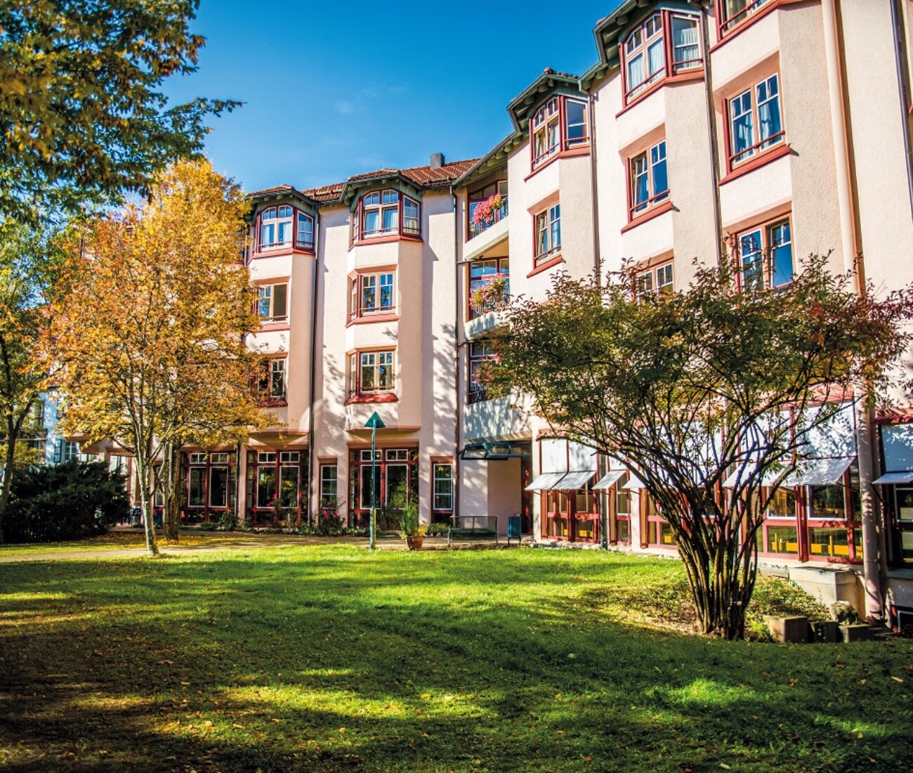 Herbstlicher Vorgarten des Bürgerheims Schwenningen mit bunten Bäumen, Sitzbank und Gehweg